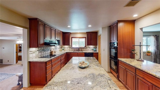 kitchen with visible vents, a sink, light stone countertops, under cabinet range hood, and black appliances