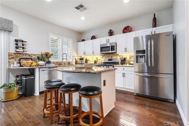 kitchen with stainless steel appliances, tasteful backsplash, dark stone counters, a kitchen bar, and white cabinets