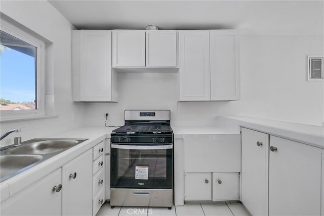 kitchen featuring light tile patterned flooring, sink, stainless steel gas range oven, backsplash, and white cabinets