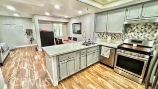 kitchen with sink, tasteful backsplash, kitchen peninsula, light hardwood / wood-style floors, and appliances with stainless steel finishes