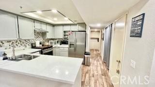 kitchen with kitchen peninsula, sink, light wood-type flooring, and appliances with stainless steel finishes