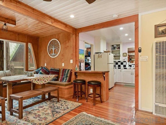 dining room with wooden ceiling, wooden walls, beamed ceiling, and light hardwood / wood-style floors