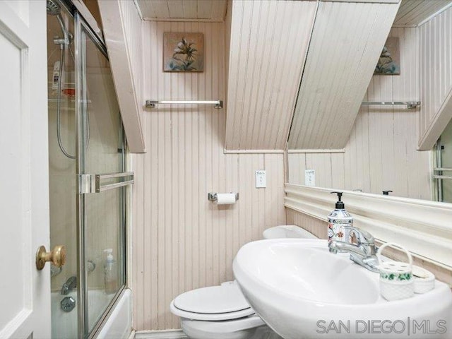 full bathroom with sink, vaulted ceiling, bath / shower combo with glass door, and wood walls