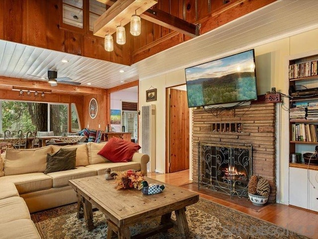 living room featuring beamed ceiling, ceiling fan, a stone fireplace, and wood-type flooring