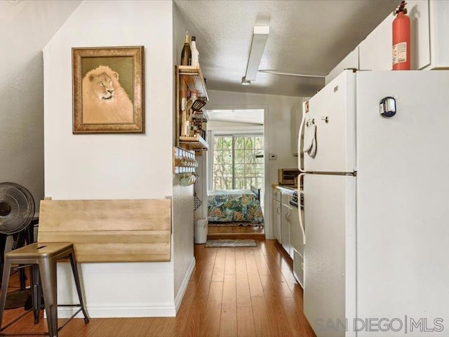 kitchen with a breakfast bar, white cabinets, white refrigerator, vaulted ceiling, and hardwood / wood-style flooring