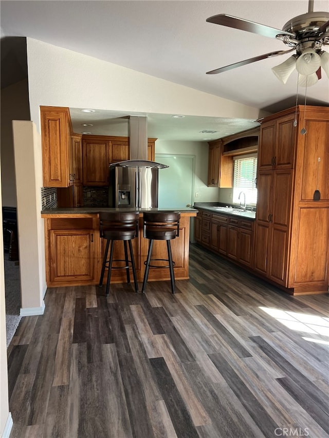 kitchen featuring kitchen peninsula, a breakfast bar, vaulted ceiling, dark wood-type flooring, and stainless steel refrigerator with ice dispenser