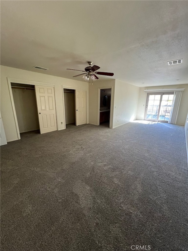 interior space with a textured ceiling, dark carpet, and ceiling fan
