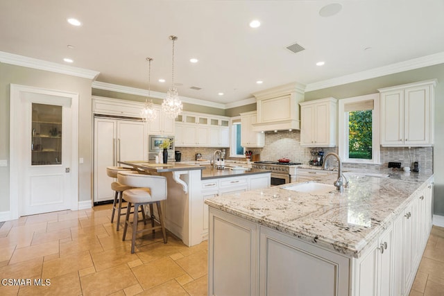 kitchen featuring a spacious island, decorative light fixtures, built in appliances, a breakfast bar, and sink