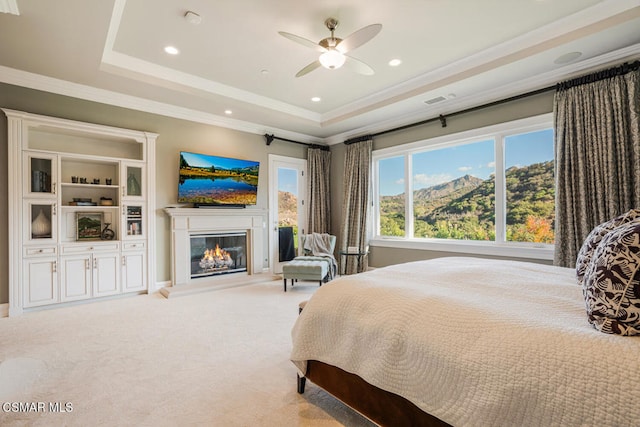 carpeted bedroom with ceiling fan, a tray ceiling, and ornamental molding