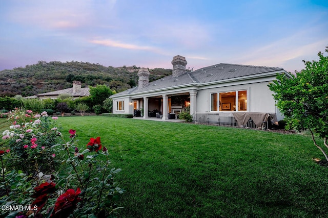 back house at dusk with a yard and a patio