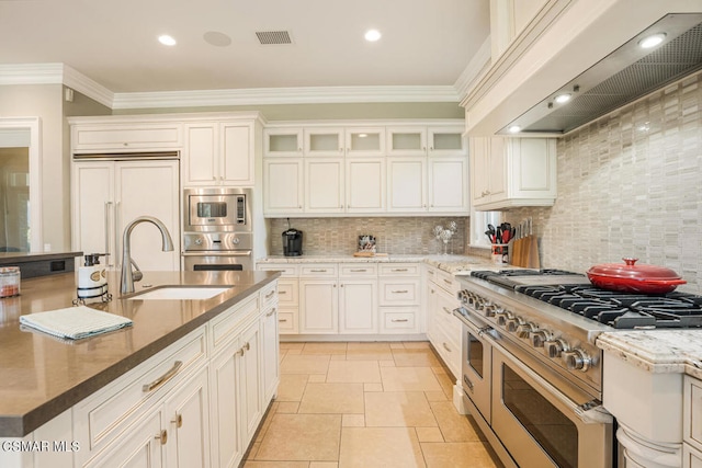 kitchen featuring tasteful backsplash, custom range hood, crown molding, built in appliances, and sink