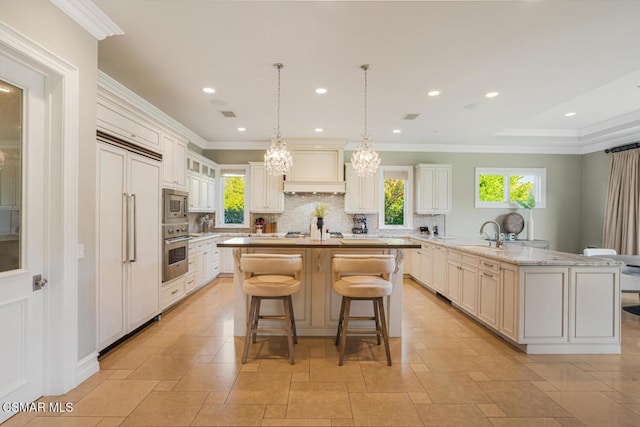 kitchen with light stone countertops, built in appliances, an island with sink, backsplash, and crown molding