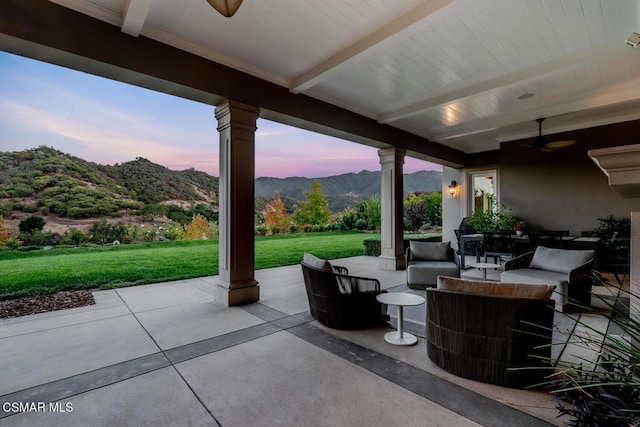 patio terrace at dusk with a mountain view, a yard, an outdoor living space, and ceiling fan