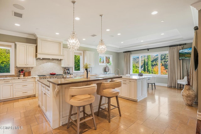 kitchen with pendant lighting, an inviting chandelier, premium range hood, backsplash, and a center island with sink