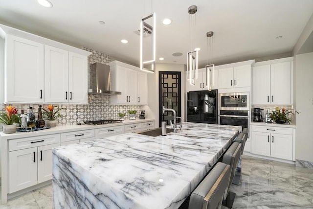 kitchen with stainless steel appliances, white cabinetry, wall chimney exhaust hood, and an island with sink