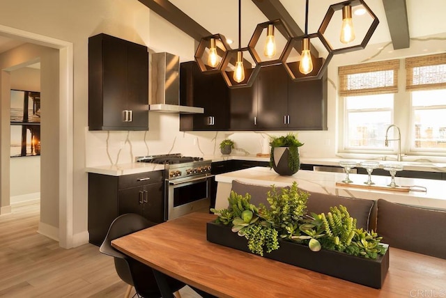 kitchen featuring hanging light fixtures, range with two ovens, light hardwood / wood-style floors, wall chimney exhaust hood, and sink