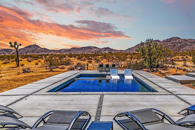 pool at dusk featuring a mountain view and a patio