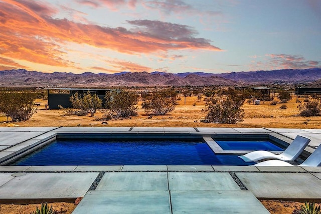 pool at dusk with a patio area, a mountain view, and an in ground hot tub