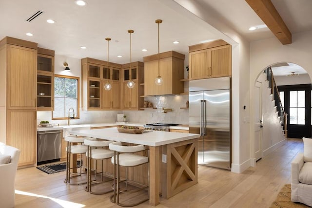 kitchen with stainless steel appliances, light hardwood / wood-style flooring, beamed ceiling, pendant lighting, and a kitchen island