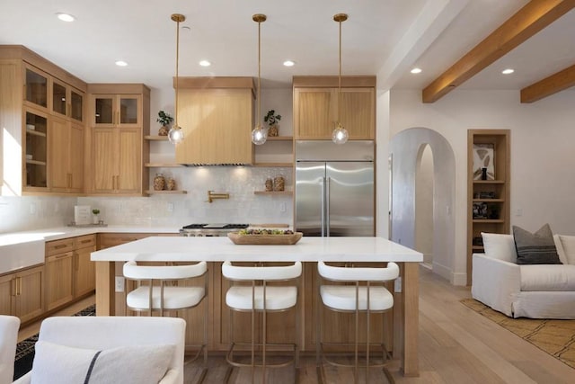 kitchen with beam ceiling, light hardwood / wood-style floors, a kitchen bar, custom range hood, and appliances with stainless steel finishes