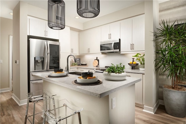 kitchen featuring white cabinetry, light hardwood / wood-style floors, appliances with stainless steel finishes, and an island with sink