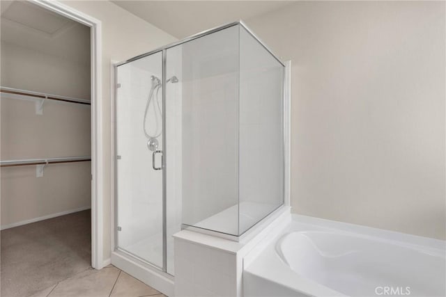 full bath with a spacious closet, tile patterned flooring, a stall shower, and a garden tub