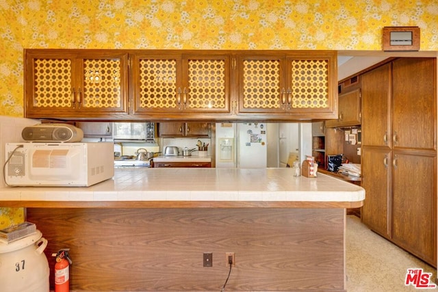 kitchen featuring light carpet, kitchen peninsula, tile counters, and white appliances