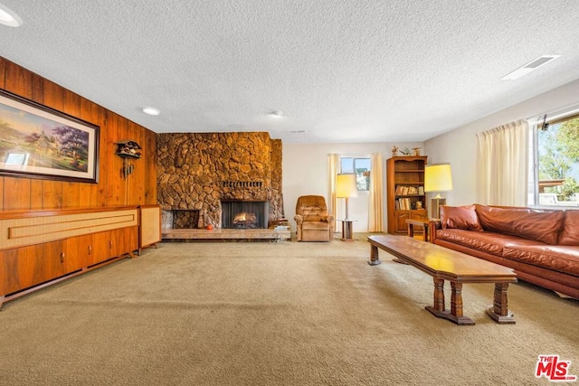 carpeted living room featuring a stone fireplace, a textured ceiling, and wooden walls