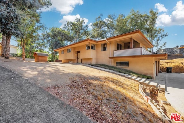 view of front of property with a storage shed and a balcony