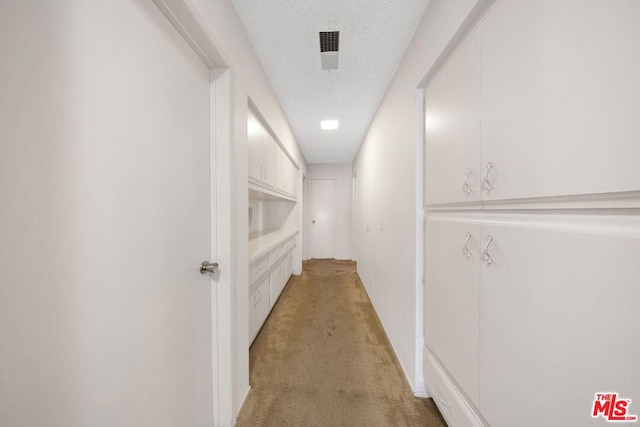 hall with a textured ceiling and light colored carpet