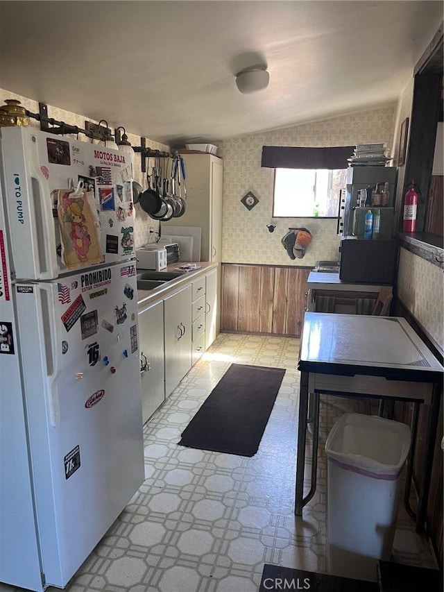 kitchen with white fridge, wooden walls, and vaulted ceiling