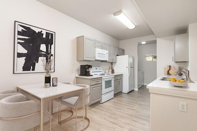 kitchen with gray cabinetry, sink, white appliances, and light hardwood / wood-style flooring