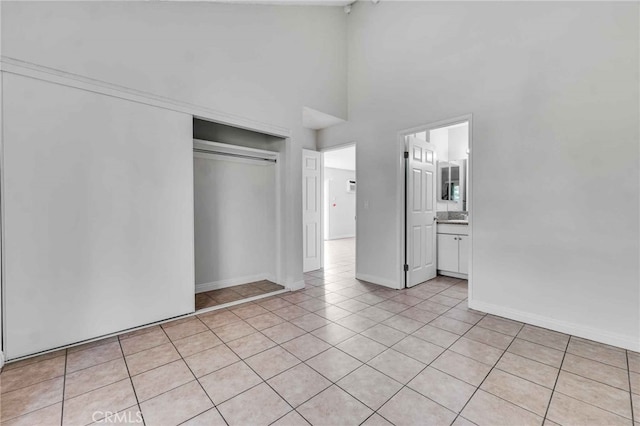 unfurnished bedroom featuring a closet, connected bathroom, a high ceiling, and light tile patterned floors