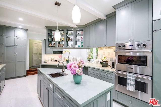 kitchen with a center island with sink, beamed ceiling, pendant lighting, double oven, and sink