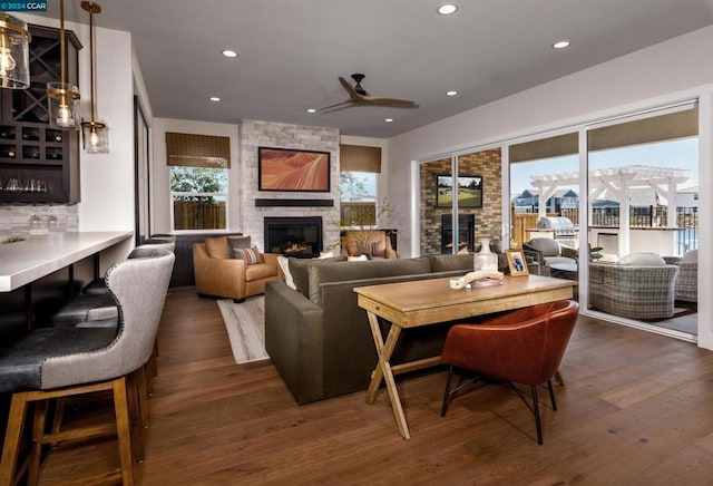 living room with a stone fireplace, dark wood-type flooring, plenty of natural light, and ceiling fan