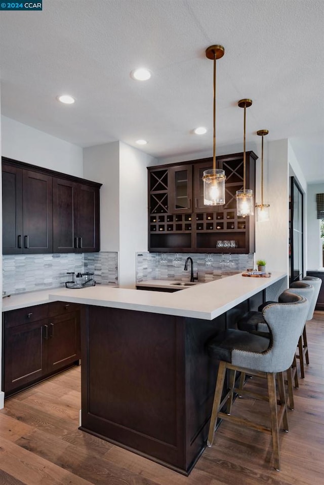 bar featuring tasteful backsplash, sink, hanging light fixtures, dark brown cabinetry, and hardwood / wood-style flooring