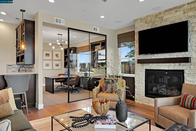 living room featuring crown molding, a stone fireplace, light hardwood / wood-style flooring, and a chandelier