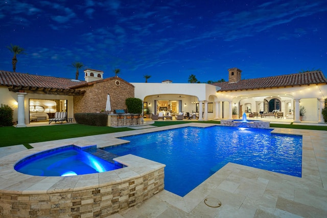 pool at twilight with a patio, pool water feature, and an in ground hot tub