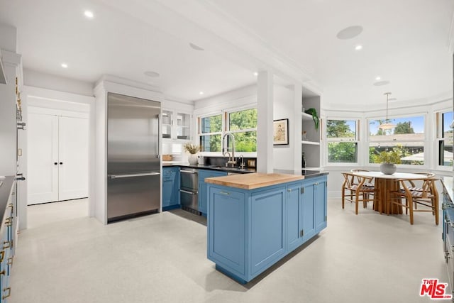 kitchen featuring appliances with stainless steel finishes, blue cabinets, sink, pendant lighting, and butcher block countertops