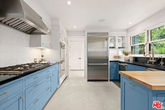 kitchen with white cabinets, sink, wall chimney exhaust hood, appliances with stainless steel finishes, and butcher block countertops