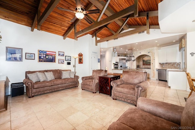 living room featuring sink, ceiling fan with notable chandelier, wood ceiling, beam ceiling, and high vaulted ceiling