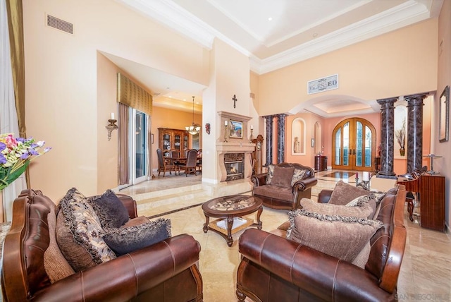 living room featuring a towering ceiling, a tray ceiling, ornate columns, crown molding, and a chandelier