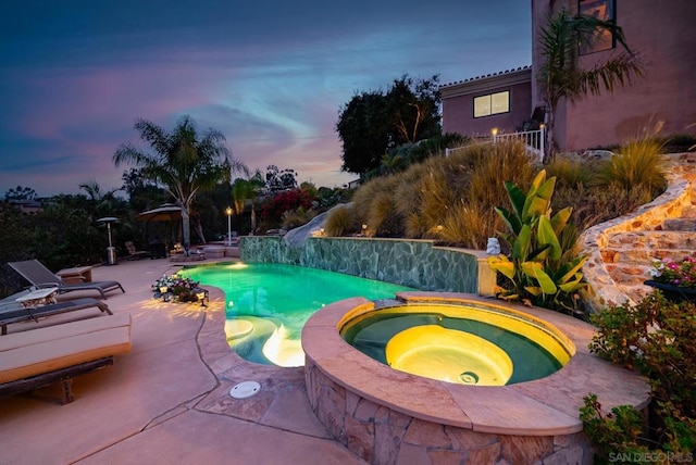 pool at dusk with an in ground hot tub, a water slide, and a patio area