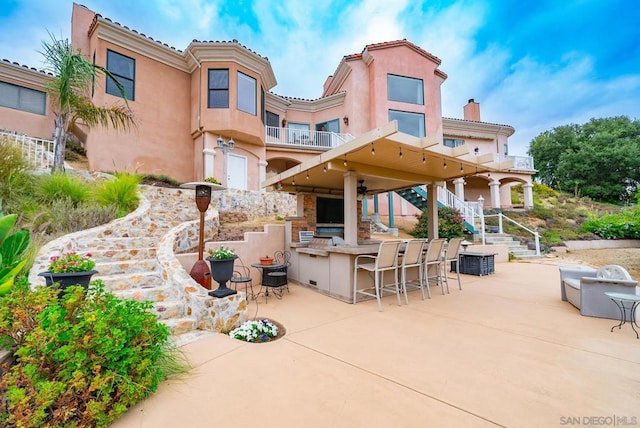 back of house featuring a balcony, exterior kitchen, exterior bar, and a patio