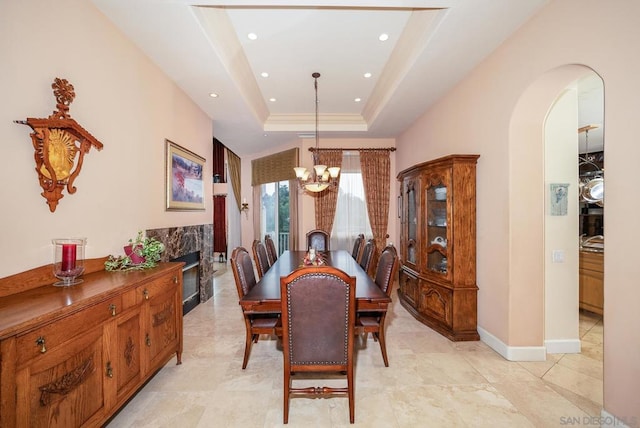 dining space with a premium fireplace, an inviting chandelier, and a raised ceiling