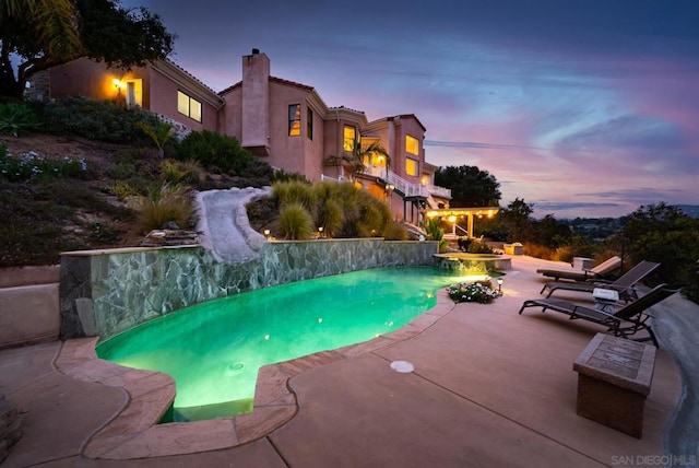 pool at dusk with a patio area and a water slide