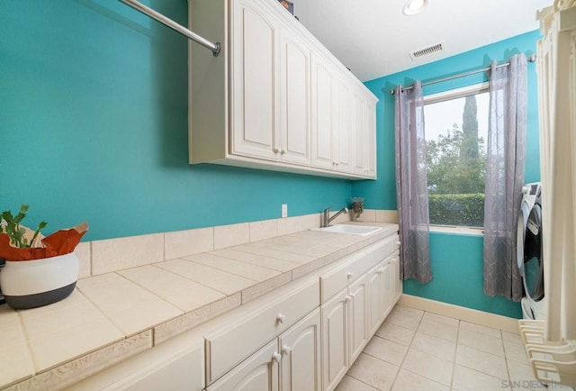 clothes washing area with sink, light tile patterned flooring, and cabinets