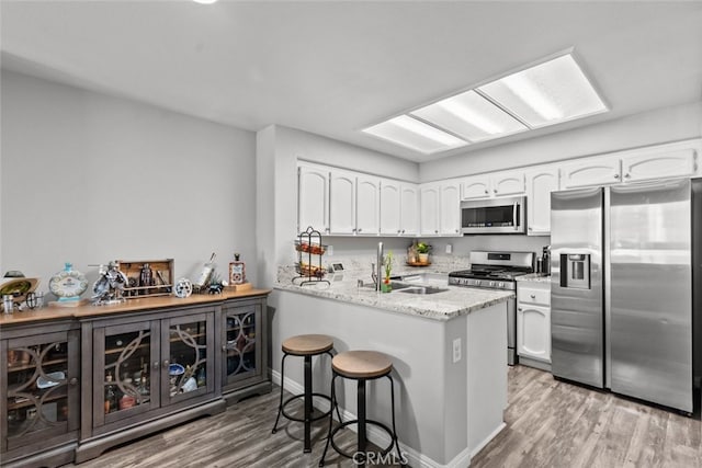 kitchen featuring stainless steel appliances, light hardwood / wood-style flooring, kitchen peninsula, and white cabinets