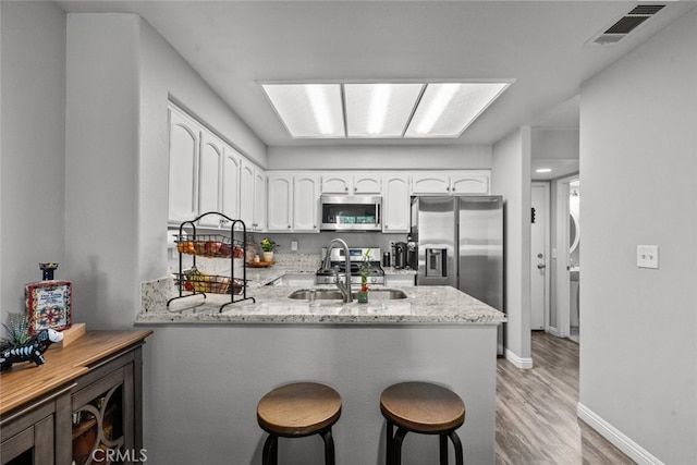 kitchen featuring kitchen peninsula, white cabinets, light wood-type flooring, appliances with stainless steel finishes, and light stone counters