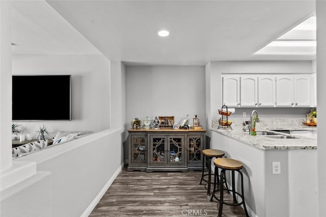 bar featuring dark wood-type flooring, light stone countertops, sink, and white cabinets